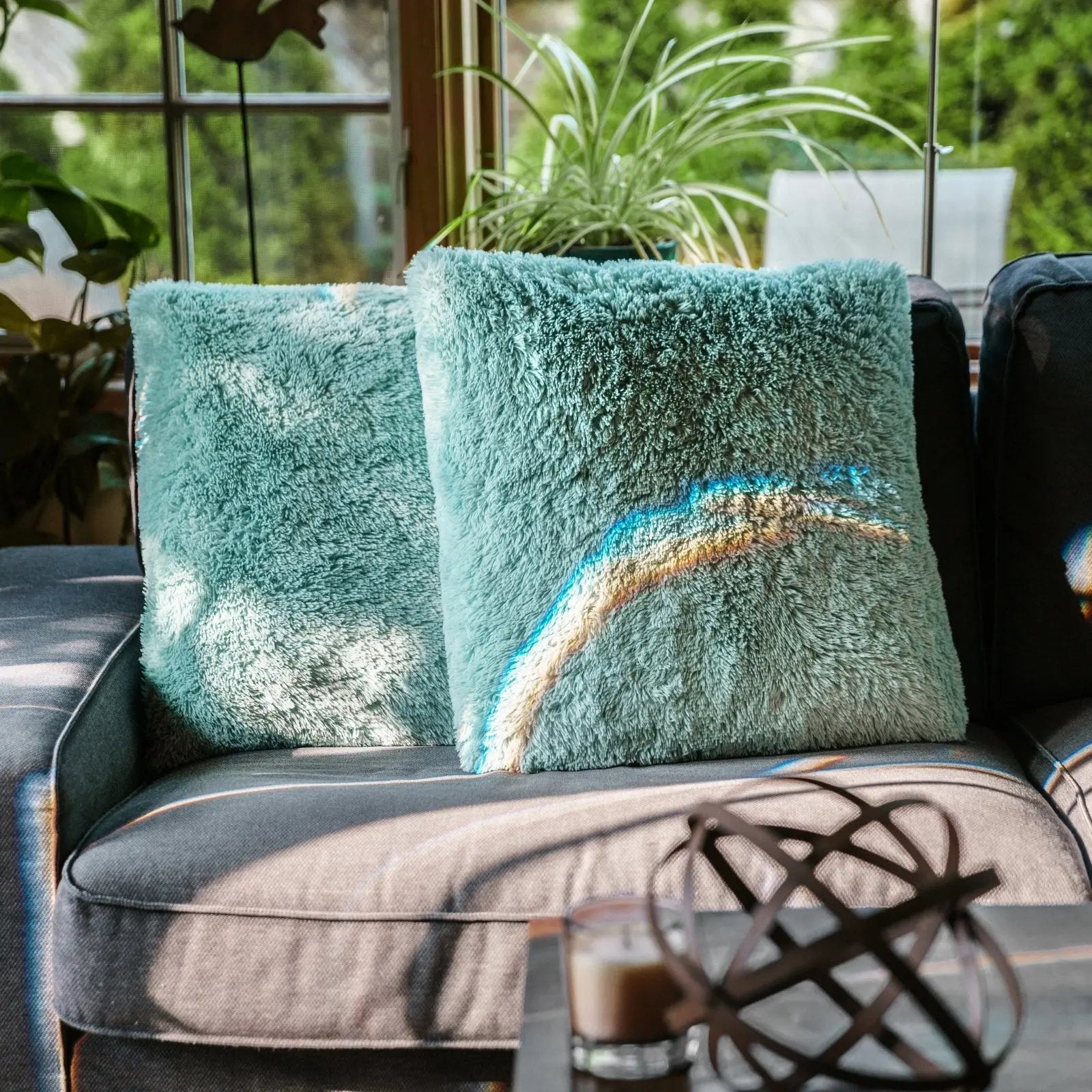 Two plush, shaggy throw pillows in a dusty teal-green color, styled on a gray fabric sofa - Direct Wicker