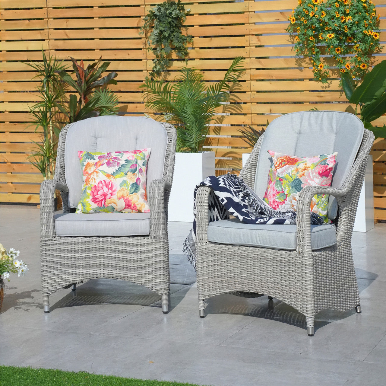 Two brown aluminum rattan armchairs with thick cushions placed outdoors, likely on a patio or garden setting.